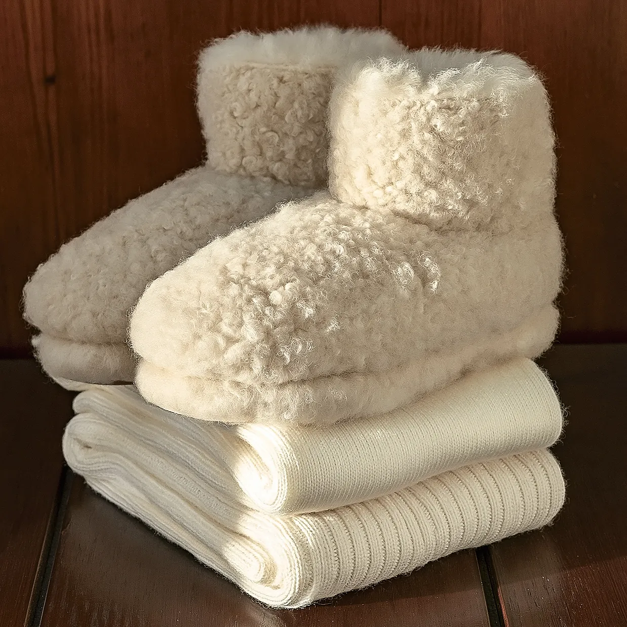 Des chaussons montants en laine bouclée ivoire, posés sur deux chaussettes côtelées pliées.